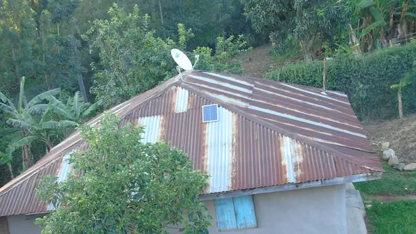 Small solar panel on the iron-sheet roof of a rural Kenyan home with a satellite dish, a typical off-grid solar setup