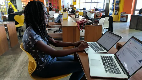 Solar data analyst in Kenya working on energy data across two laptops